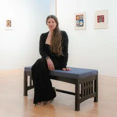 An art student sitting on a bench in a g所有ery. The exibit around her features her artwork.